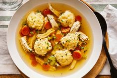 a white bowl filled with chicken and dumplings on top of a wooden table next to a glass of water