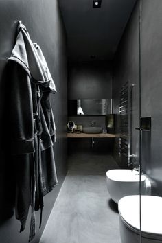 a black and white photo of a bathroom with two toilets, a sink and a towel hanging on the wall