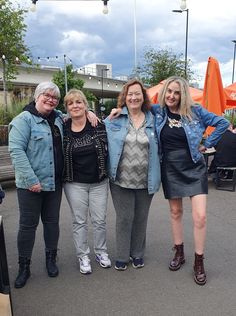 three women standing next to each other in front of an orange umbrella covered park area