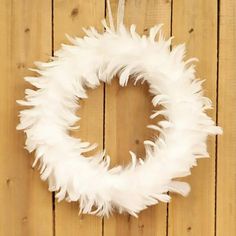 a white feather wreath hanging on a wooden wall with the letter o in the middle