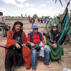 three men sitting on the ground in front of a group of people with hats and scarves