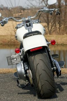 a white and black motorcycle parked on the road next to a body of water with trees in the background