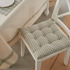 a white chair with a checkered seat cushion next to a dining table and place setting