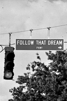 black and white photograph of street sign that says follow that dream mars above traffic lights