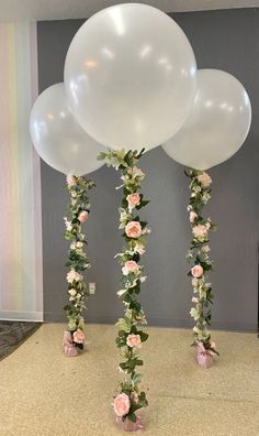 three white balloons with flowers and greenery on the bottom are standing in front of a wall