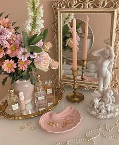 a table topped with pink and white flowers next to a gold frame filled with perfume bottles