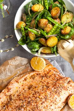 a plate of fish, salad and lemon wedges on a wooden cutting board next to a glass of water