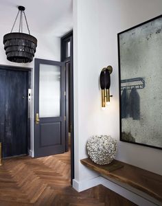 an instagramted photo of a hallway with wood floors and white walls, black doors and chandelier