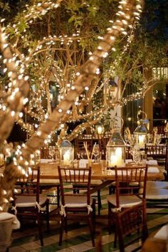 an outdoor dining area is lit up with fairy lights and decorated trees for the centerpieces