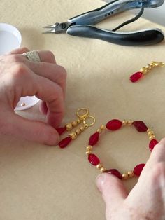 someone is making beaded bracelets with gold and red glass beads on a table