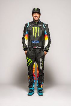 a man standing in front of a gray background wearing a black and blue racing suit