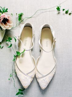 two pairs of white shoes sitting on top of a table next to a pink flower