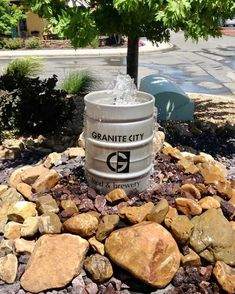 a trash can sitting on top of a pile of rocks next to a small tree