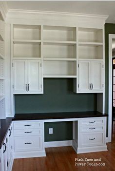 an empty room with white cabinets and black counter tops in the center, along with wood flooring