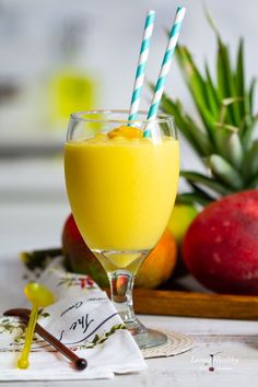 an orange juice in a glass with two straws next to it and some fruit on the table