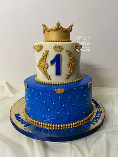 there is a blue and white cake with gold decorations on the top, along with a crown