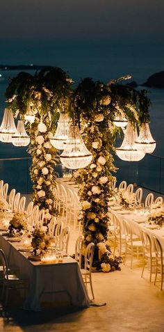 an outdoor dining area with white chairs and tables set up for dinner on the water