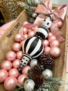 christmas ornaments in a wooden box with pink balls and pine cones on the bottom, one black and white striped ornament