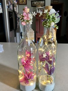 two glass bottles with flowers in them sitting on a counter top next to each other