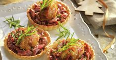 three small tarts with meat and vegetables on a white platter next to bread