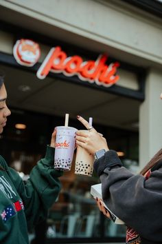 two young women standing in front of a fast food restaurant holding drinks and looking at each other