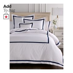 a bed with white and blue comforters on top of it, next to a night stand