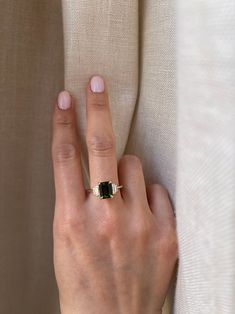 a woman's hand with a gold ring on her finger and a white curtain in the background