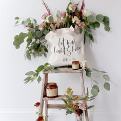 a white bag sitting on top of a wooden step ladder next to flowers and candles