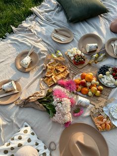 an outdoor picnic with plates and food on the ground, including fruit, cheeses, crackers, and flowers