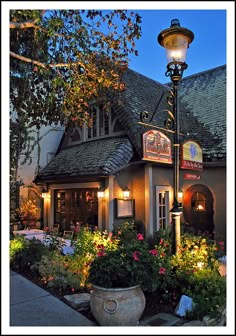 the front of a restaurant lit up at night with flowers in pots and potted plants