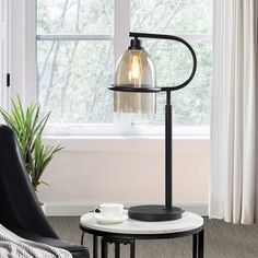 a table with a lamp on it next to a chair in front of a window