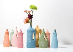 a vase filled with flowers next to several different colored plastic bottles on a white surface