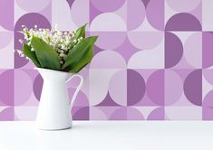 a white vase filled with flowers on top of a table next to a purple wall