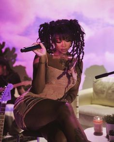 a woman with dreadlocks sitting on a chair while holding a microphone in her hand