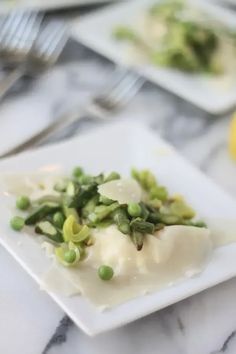 a white plate topped with green vegetables next to a lemon wedge and silverware on a marble table