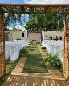 an outdoor ceremony setup with white linens and greenery on the ground, surrounded by wooden arbors