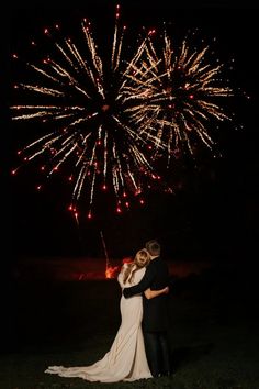 a bride and groom embrace as fireworks go off in the background