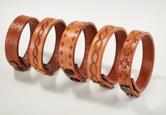 four wooden bracelets are lined up against a white background, each with an intricate design