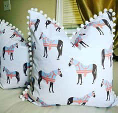 two pillows with horses and pom poms on them