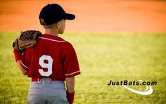 a young boy wearing a catchers mitt standing in the outfield at a baseball game