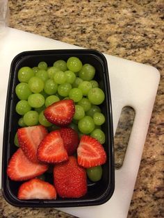 grapes and strawberries in a plastic container on a cutting board