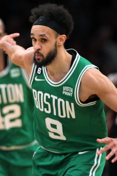 two boston basketball players in green uniforms are on the court and one is holding his hand out