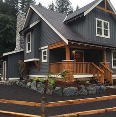 a gray house with white trim and wood accents on the front porch is surrounded by trees