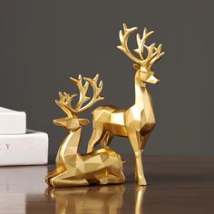 two golden deer figurines sitting on top of a table next to a white box