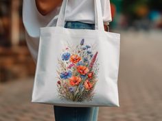 "Step out in style with our \"Summer Blossom Watercolor Tote,\" where functionality meets the splendor of summer gardens. Adorned with a lush display of wildflowers, this tote showcases stunning watercolor artistry with poppies and cornflowers in vivid shades of orange, pink, and blue. Each brushstroke celebrates the delicate textures and gradients only achievable with watercolor techniques, giving life to this 100% cotton canvas tote. The robust self-fabric handles provide comfort and resilience for daily use, while the generous 15\"x16\" size ensures you have ample space for your essentials. Printed using state-of-the-art Direct-to-Garment technology, the colors remain radiant wash after wash, making this bag a durable piece of art. Perfect for those who value eco-friendly fashion, this Spring Travel Canvas Bag, Spring Vacation Canvas Bag, Summer Floral Print Travel Bags, Summer Travel Bags With Floral Print, Spring Travel Canvas Bag With Floral Print, Spring Canvas Shopping Bag, Spring Shopping Canvas Bag, Summer Floral Print Tote Bag, Summer Floral Print Bags For Daily Use