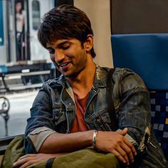 a man sitting on a train looking at his cell phone and smiling while he sits down