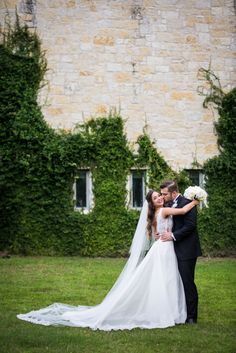 a bride and groom standing in front of a stone building with ivy growing around it