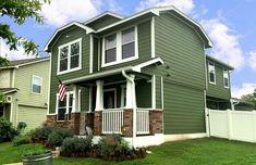 a house with green siding and white trim on the front porch, fenced in yard