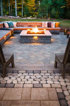 an outdoor fire pit surrounded by benches and seating area with lights on each end in front of it