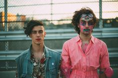 two men standing next to each other in front of a fence with their faces painted pink and blue